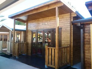 A wooden DIY kit homes building with a sign labeled "darfield" above the entrance, featuring double glass doors and a small porch-like area. Phoenix Patios, Cottages and Granny Flats in Perth